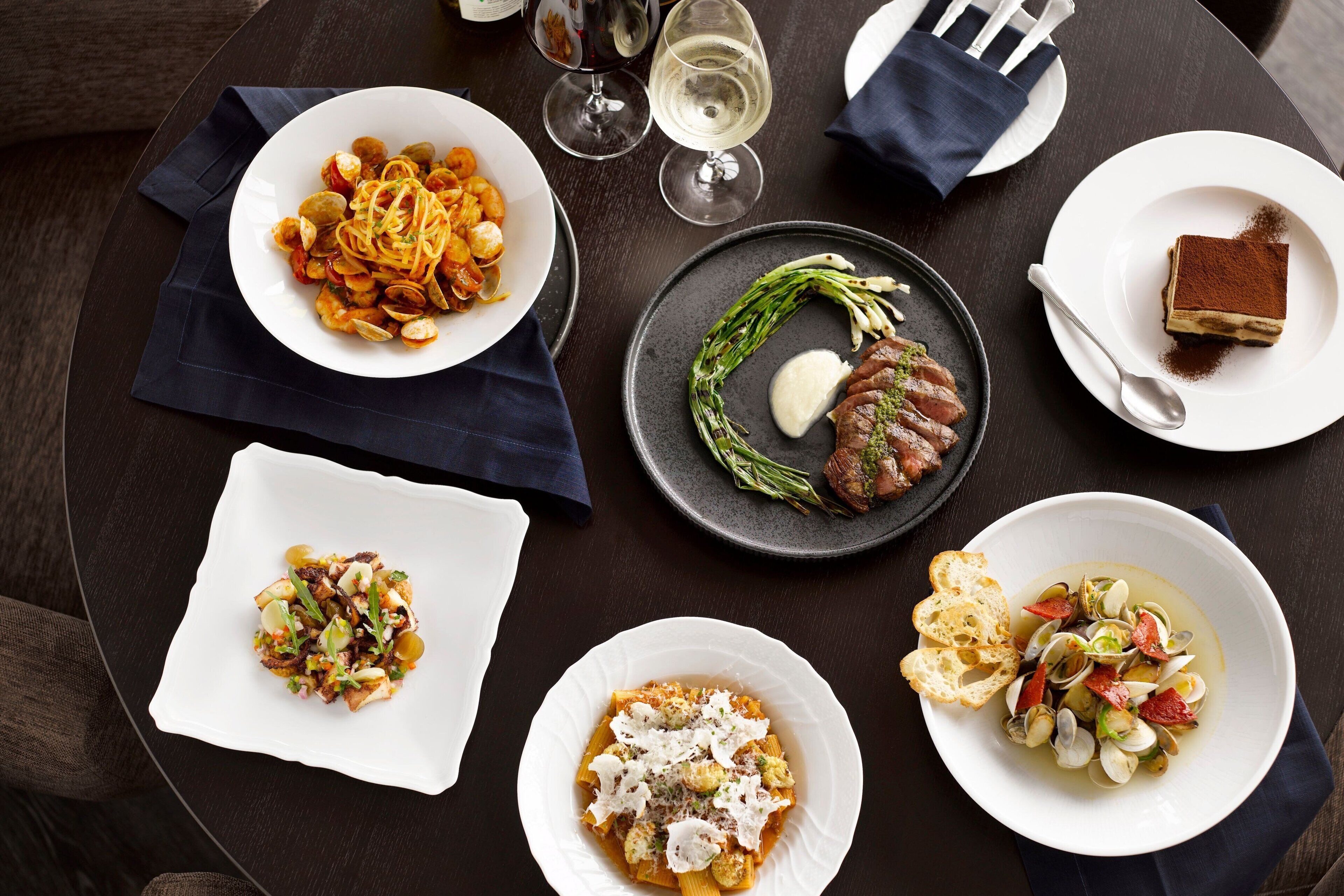 A dining table with various dishes, including pasta, steak, and a dessert.