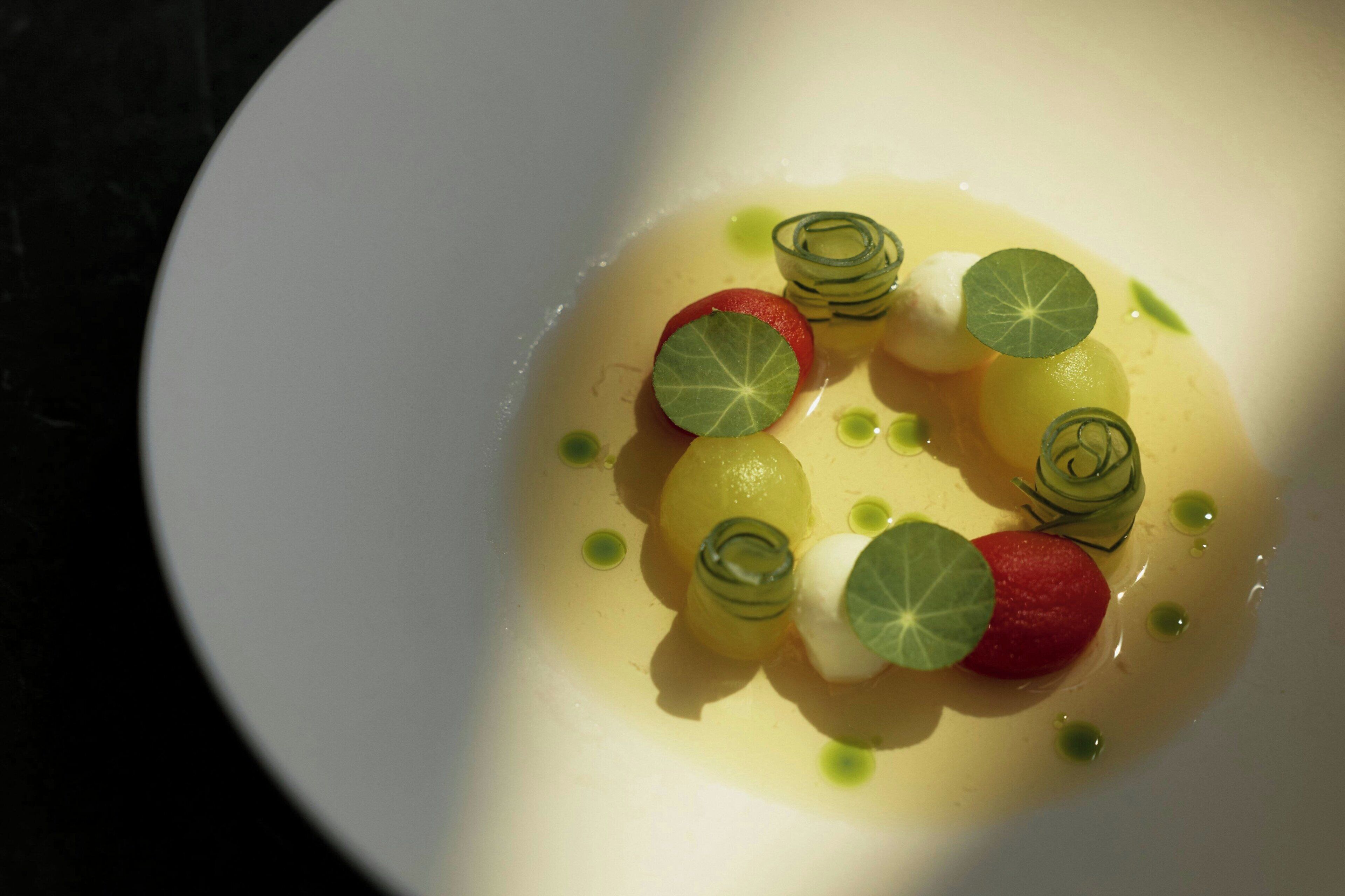 A white plate with a dessert featuring spherical shapes and green garnishes.
