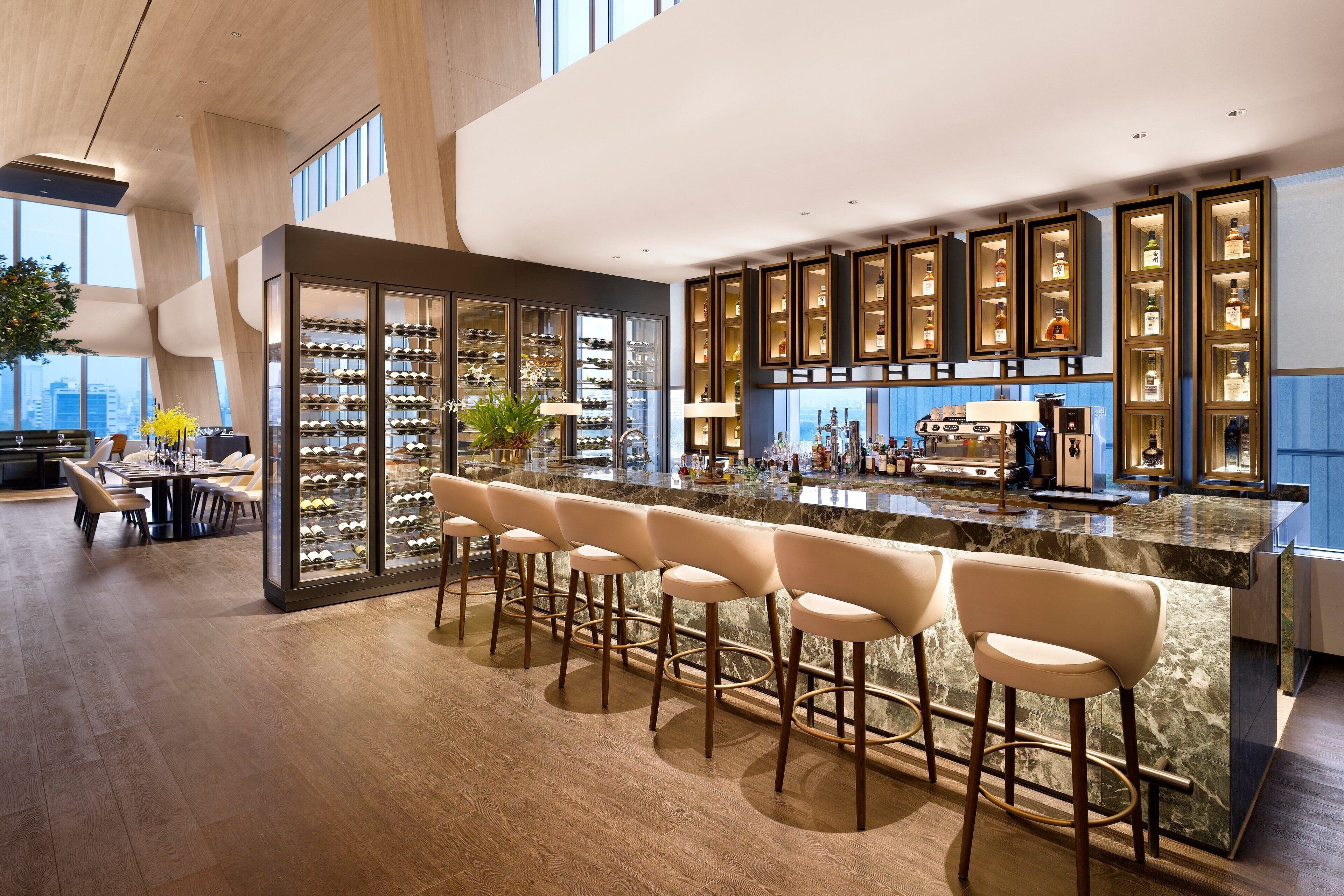A modern bar area with a marble countertop, bar stools, and a wine display.