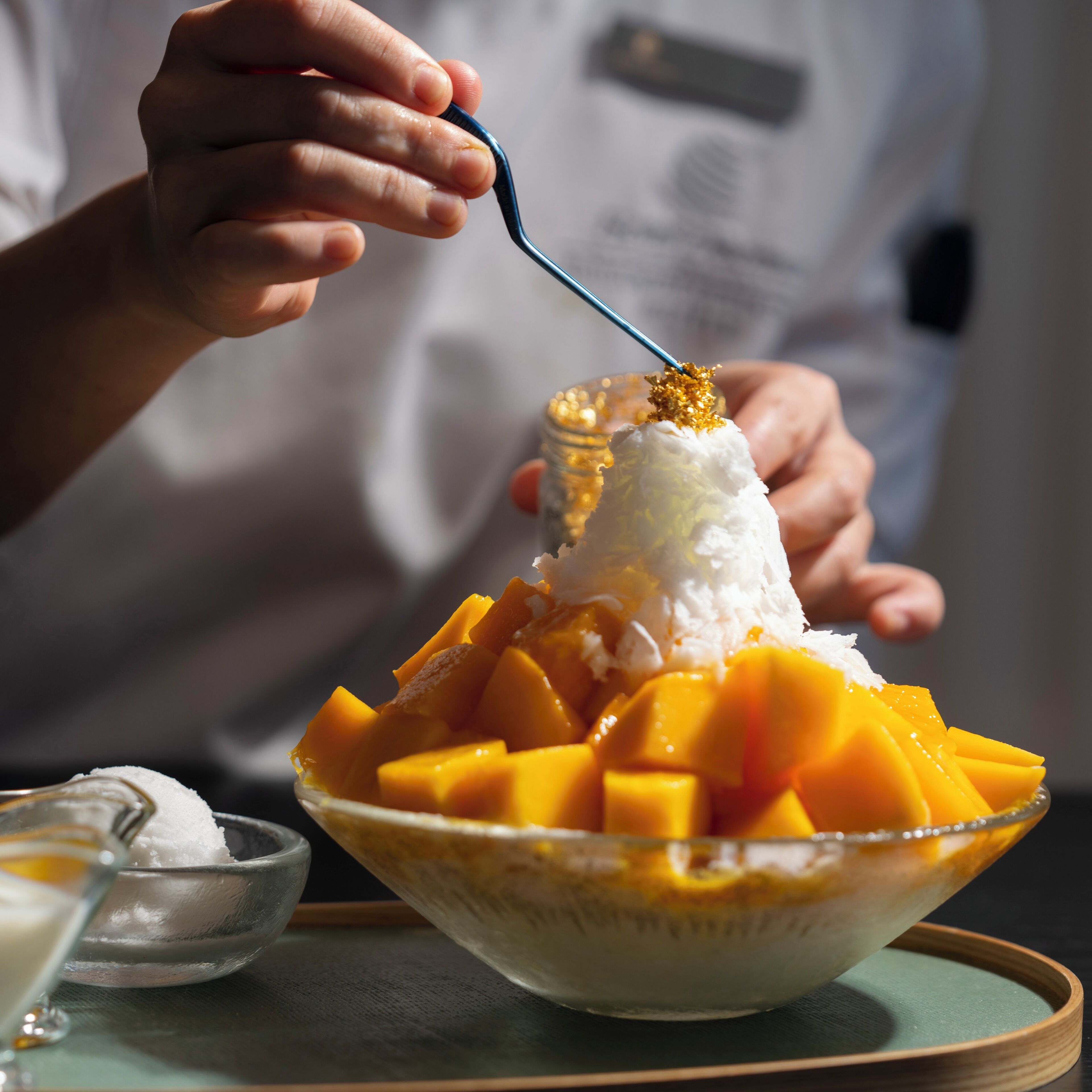 En skål med hyvlad is, garnerad med mangobitar och en sked.