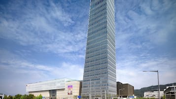 A tall, modern skyscraper with a glass facade, surrounded by other buildings and a clear sky.