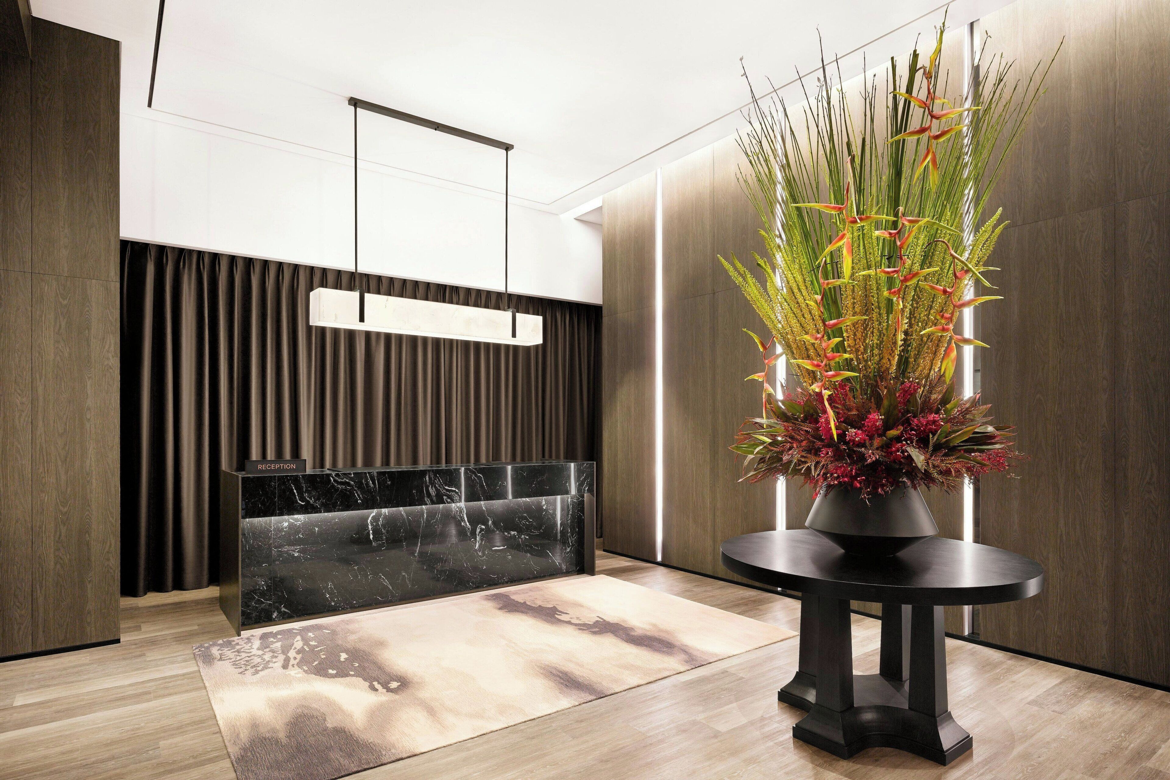 A reception area with a marble counter, a modern hanging light fixture, and a potted plant with red flowers.