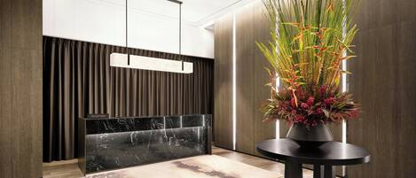 A reception area with a marble counter, a modern hanging light fixture, and a potted plant with red flowers.