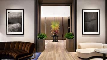 A modern lobby with a brown sofa, a cream-colored sofa, and a table with a vase of flowers. There are two framed artworks on the walls.