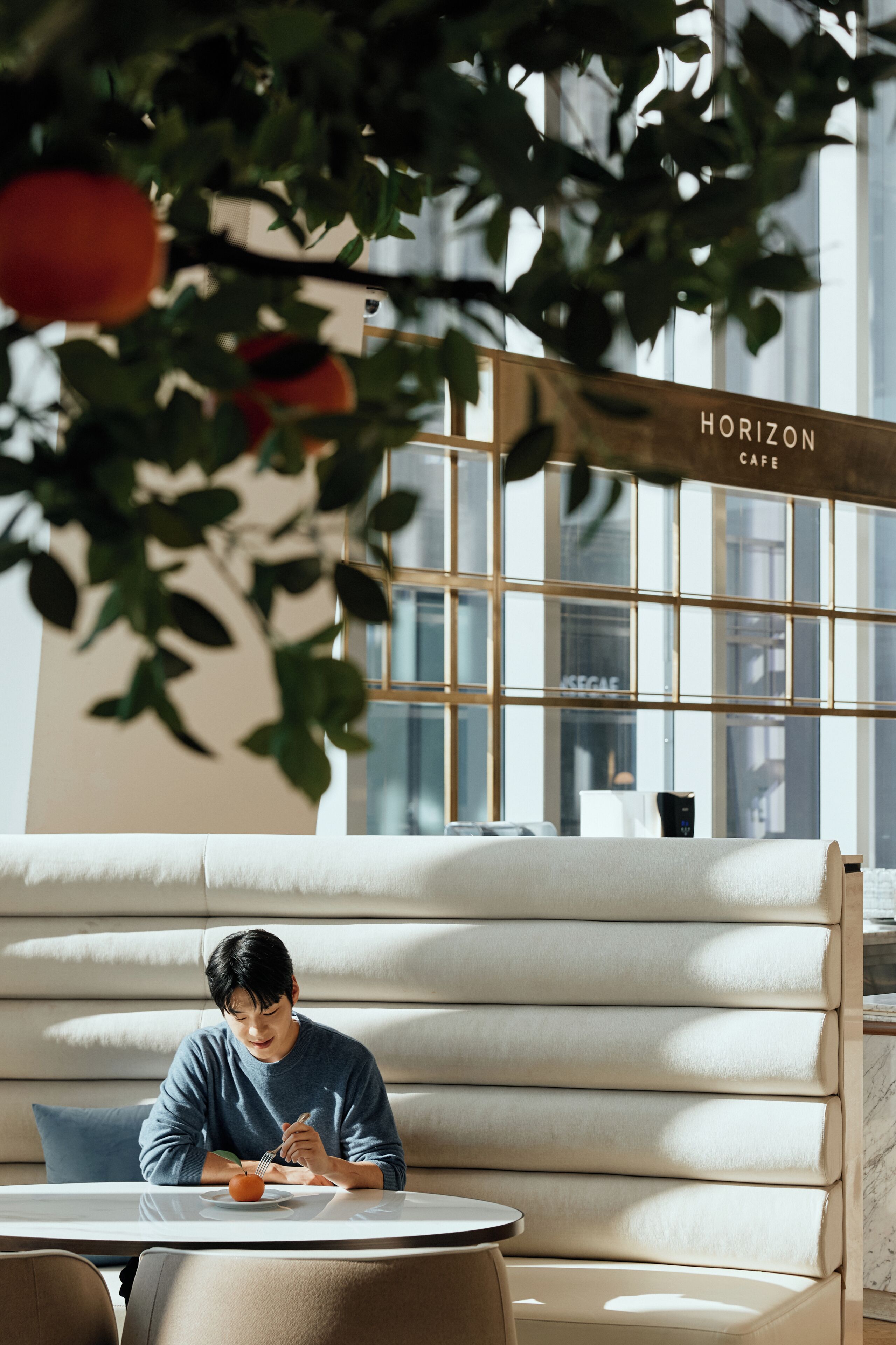 A person sitting at a table with a plate of food, a couch, and a sign that reads 'HORIZON CAFE' in the background.