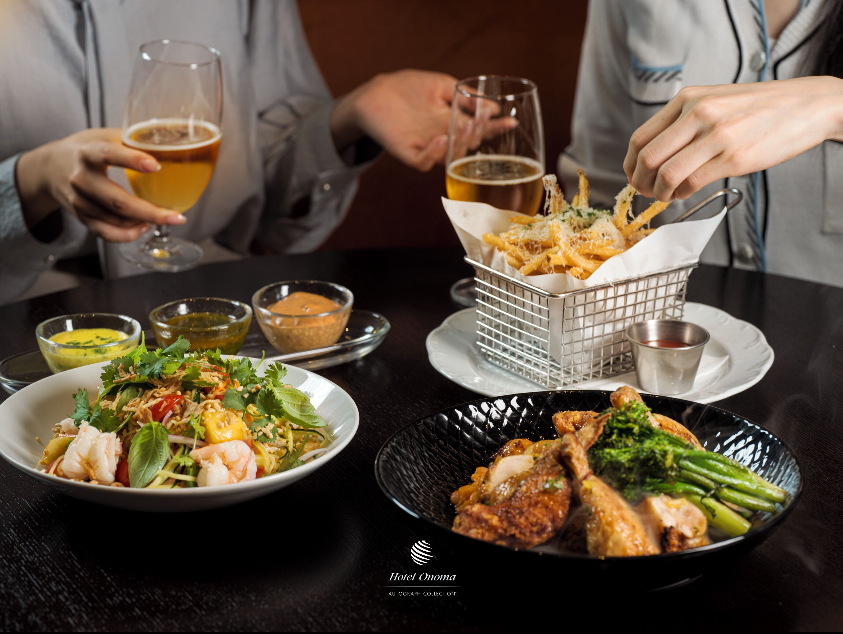 A dining table with various dishes, including seafood, fries, and a salad, along with glasses of beer.