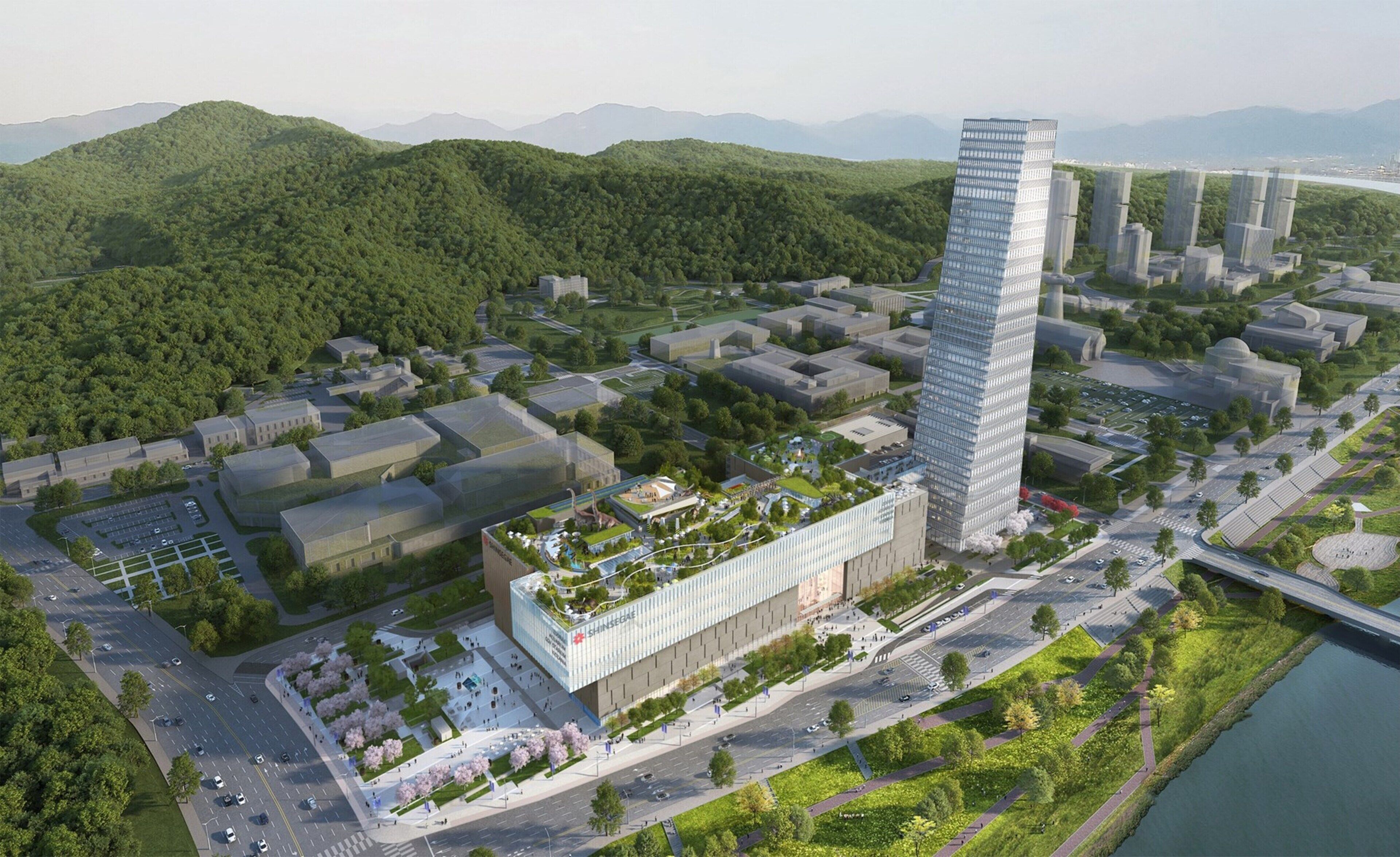 A modern high-rise building with a glass facade, surrounded by greenery and a river.