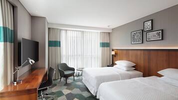 Habitación de hotel con dos camas, un escritorio con silla, televisor y ventana con cortinas.