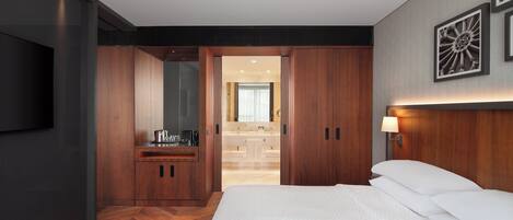 Una habitación de hotel moderna con una cama grande, un armario de madera y un televisor montado en la pared.