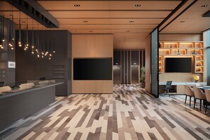 Un hall d’hôtel moderne comprenant un comptoir d’accueil, un espace salon et un grand téléviseur à écran plat.