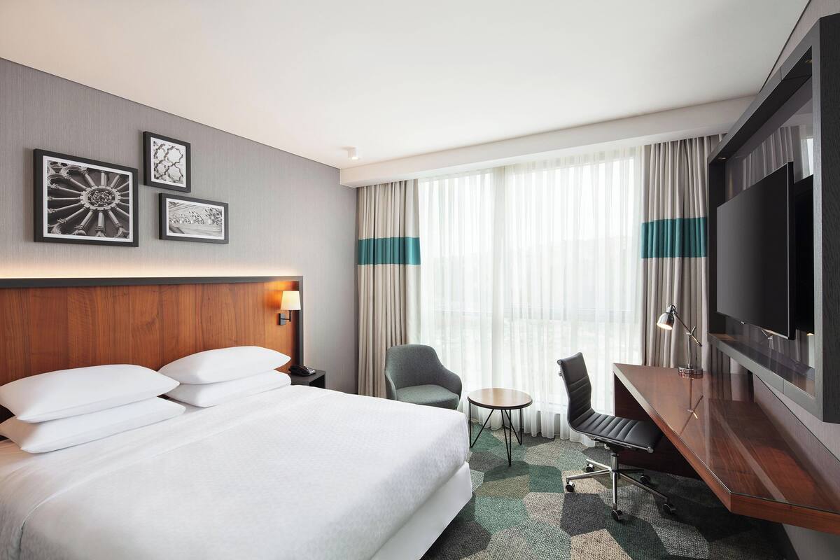 Habitación de hotel con una cama grande, un escritorio, una silla, un televisor y obras de arte en la pared.