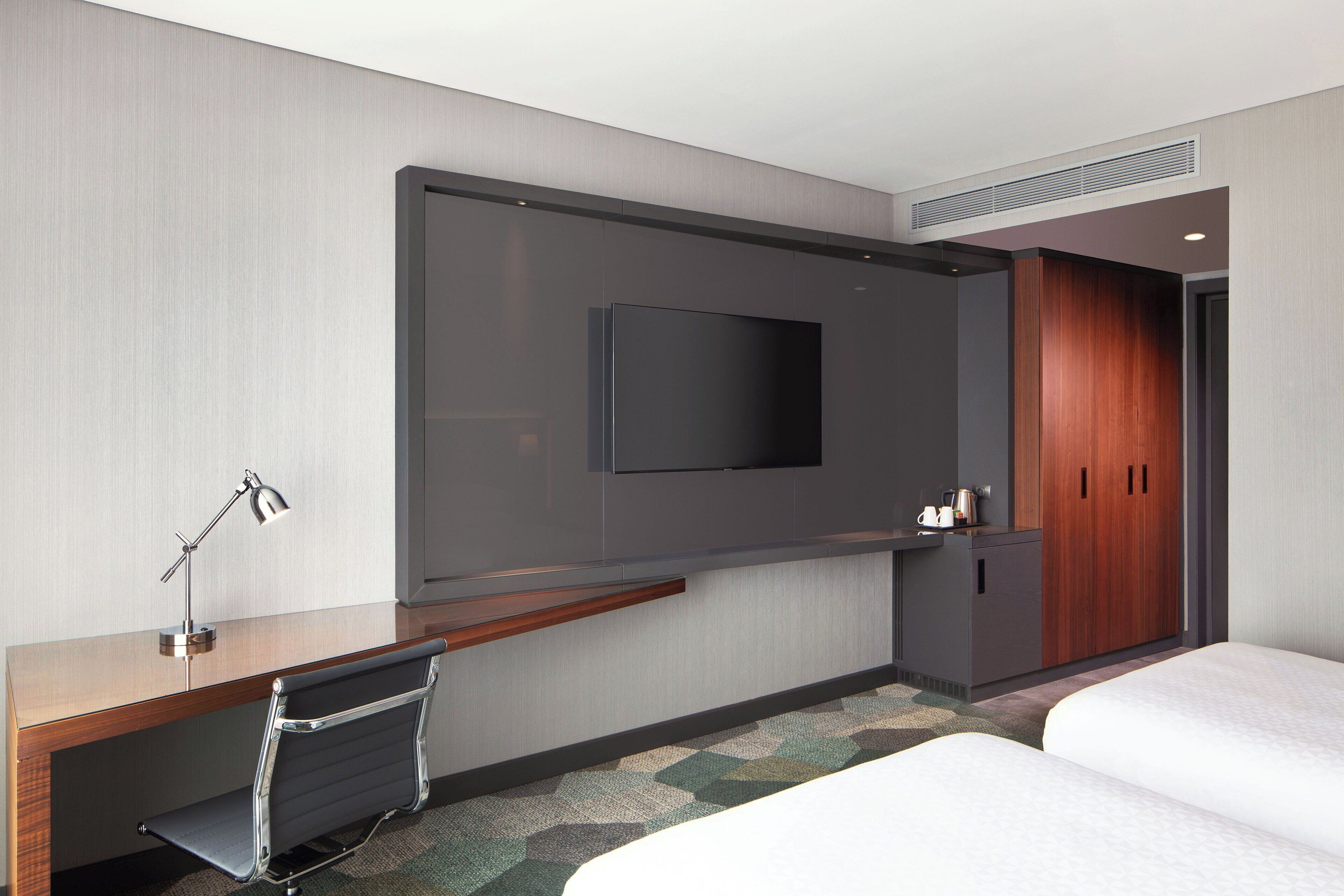 Une chambre d’hôtel équipée d’un téléviseur à écran plat fixé au mur, d’un bureau en bois avec une chaise, d’un lit et d’une armoire.