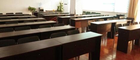 A conference room with rows of tables and chairs, a whiteboard, and a large window with curtains.