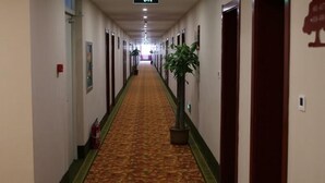 A long, carpeted hallway with doors on both sides, a fire extinguisher on the left, and a potted plant in the center. - Greentree Inn Dezhou Kangbo Avenue Statium Express Hotel (Dezhou)