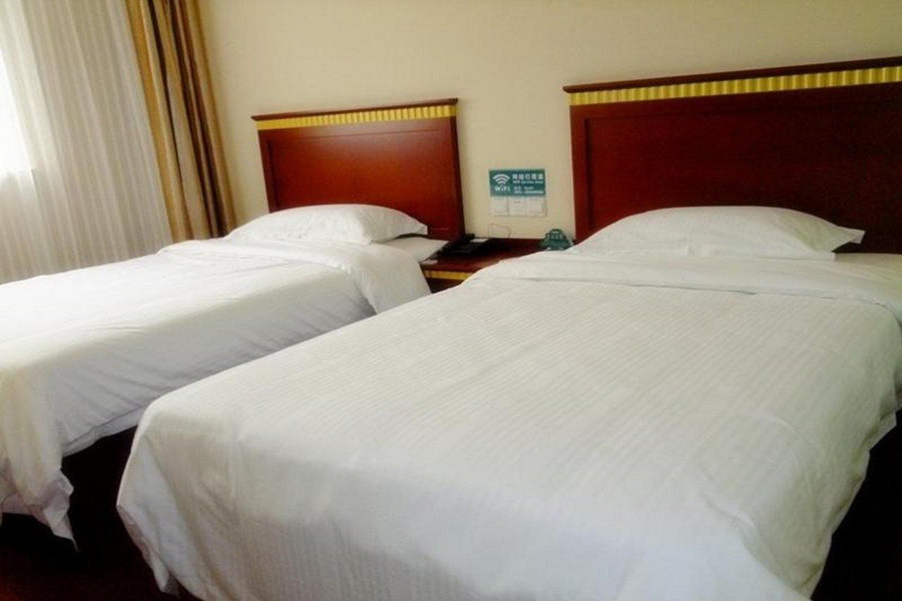 A hotel room with two single beds, a wooden headboard, a nightstand, and a sign indicating Wi-Fi availability.