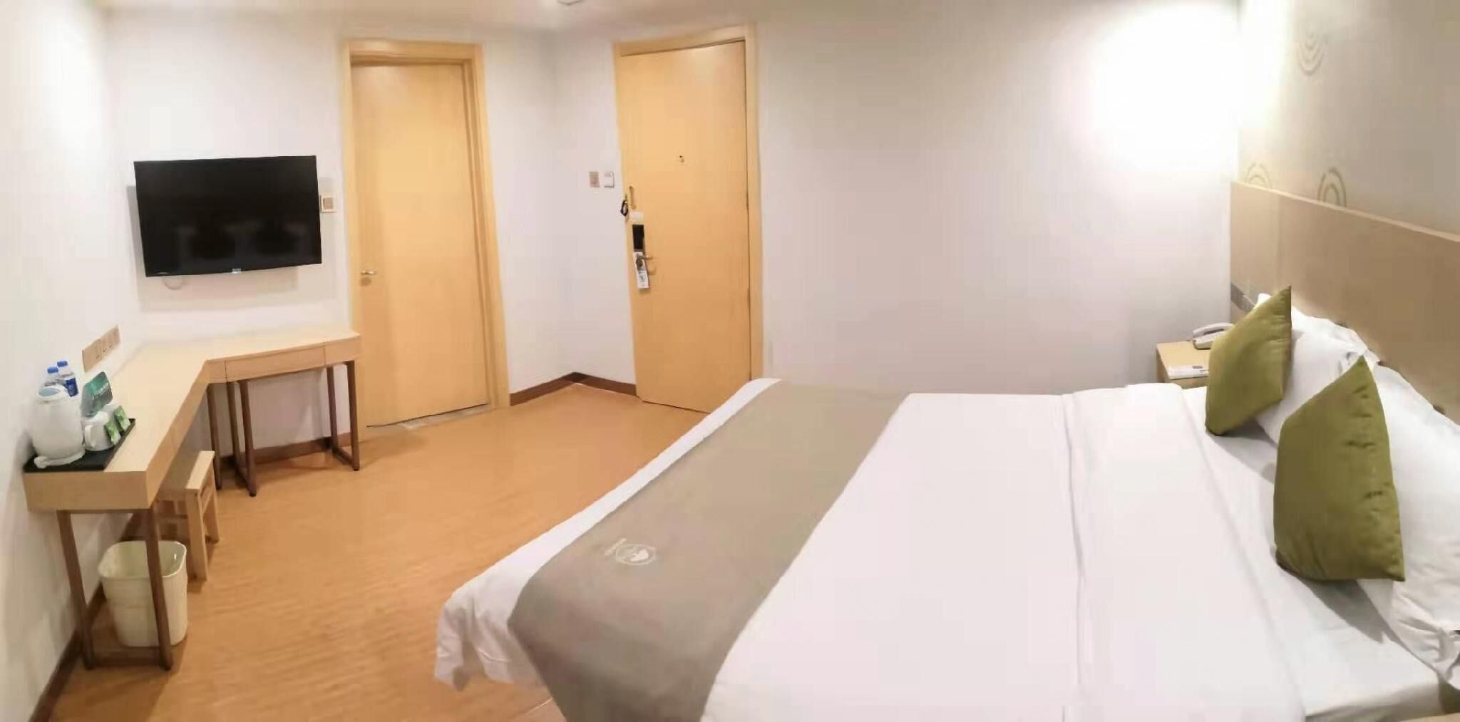A hotel room with a bed, a desk, a chair, a television, and two doors.