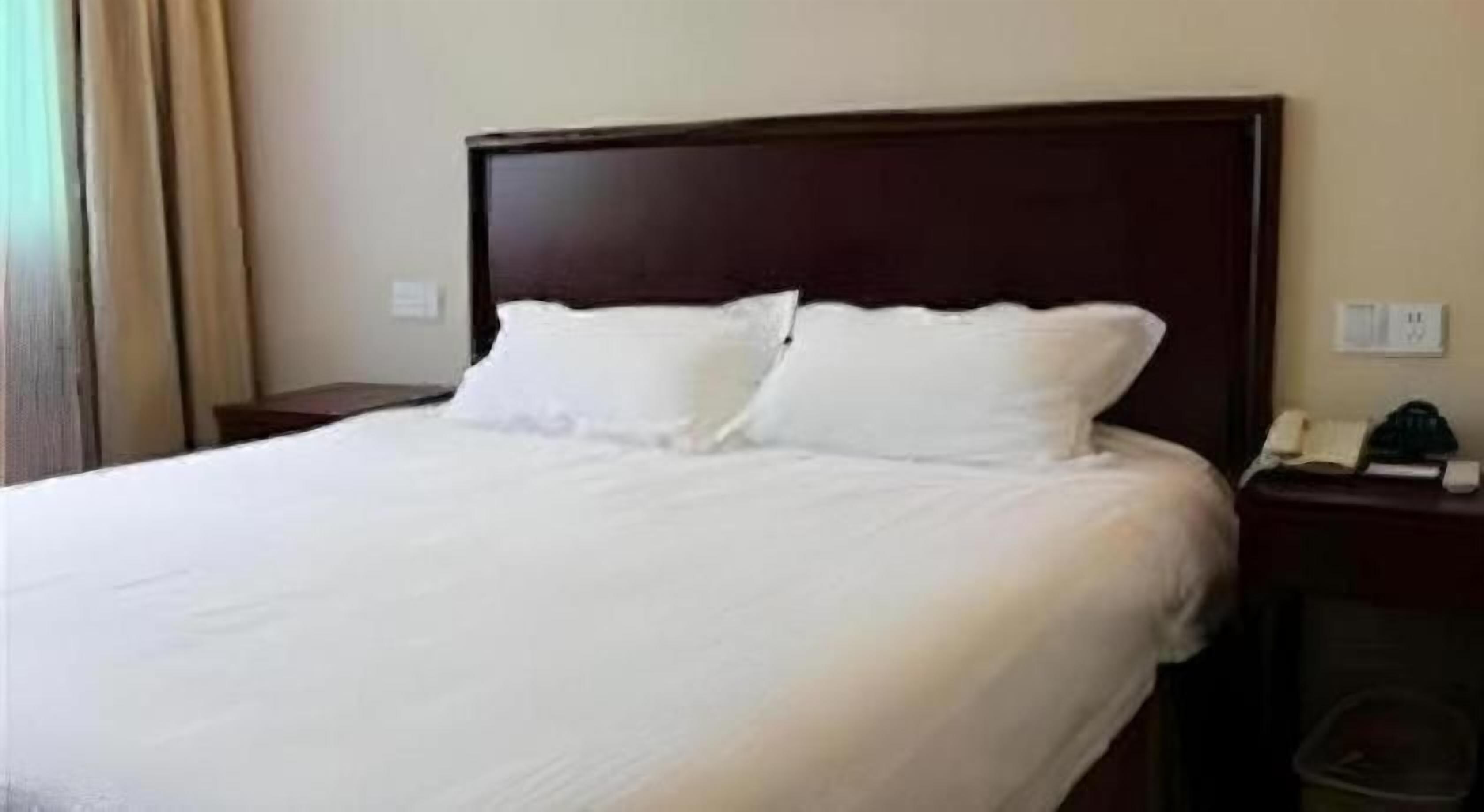A hotel room with a large bed, a wooden headboard, a nightstand with a telephone, and a wall socket.