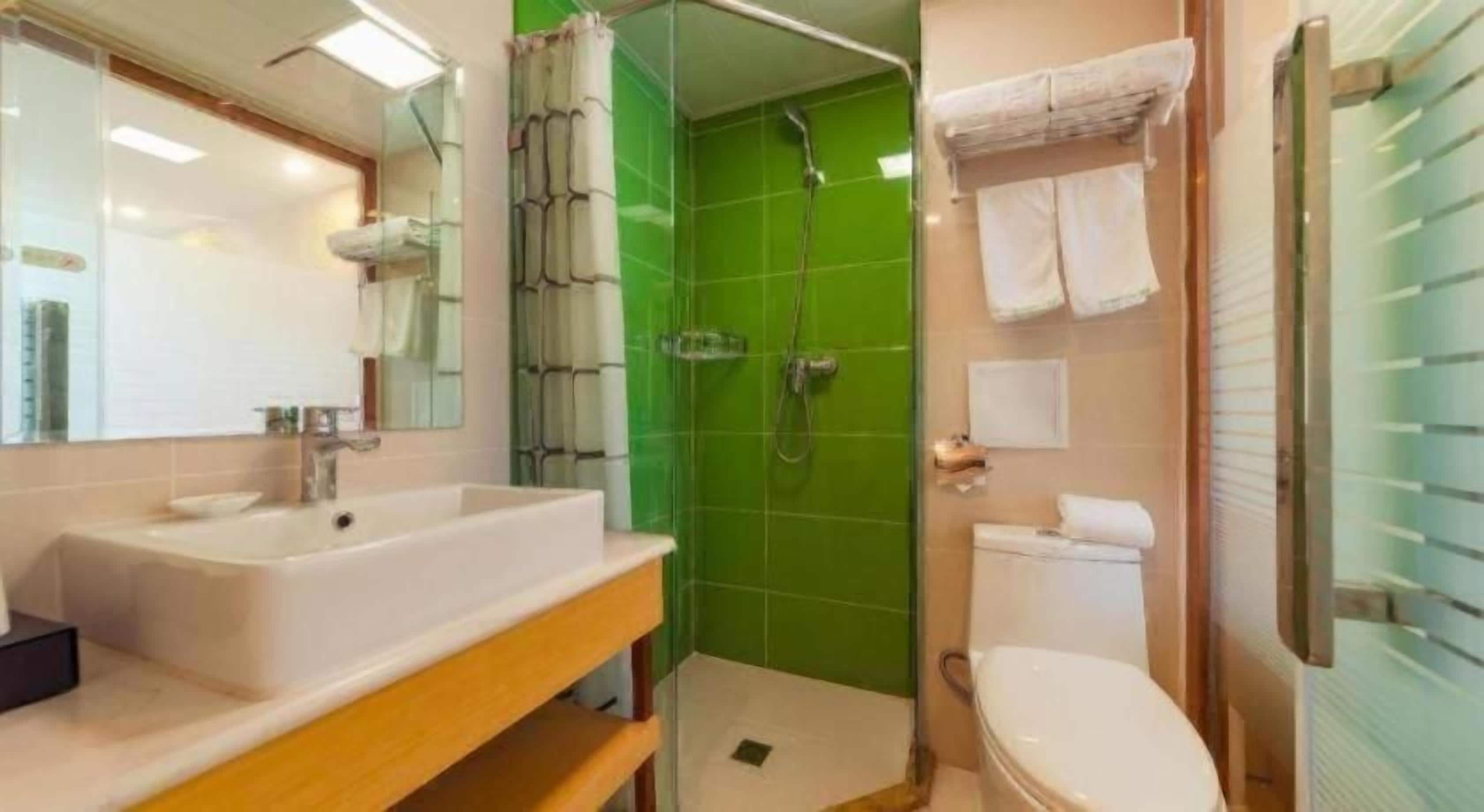 Un baño con un lavamanos blanco, un espejo y un box de ducha verde.