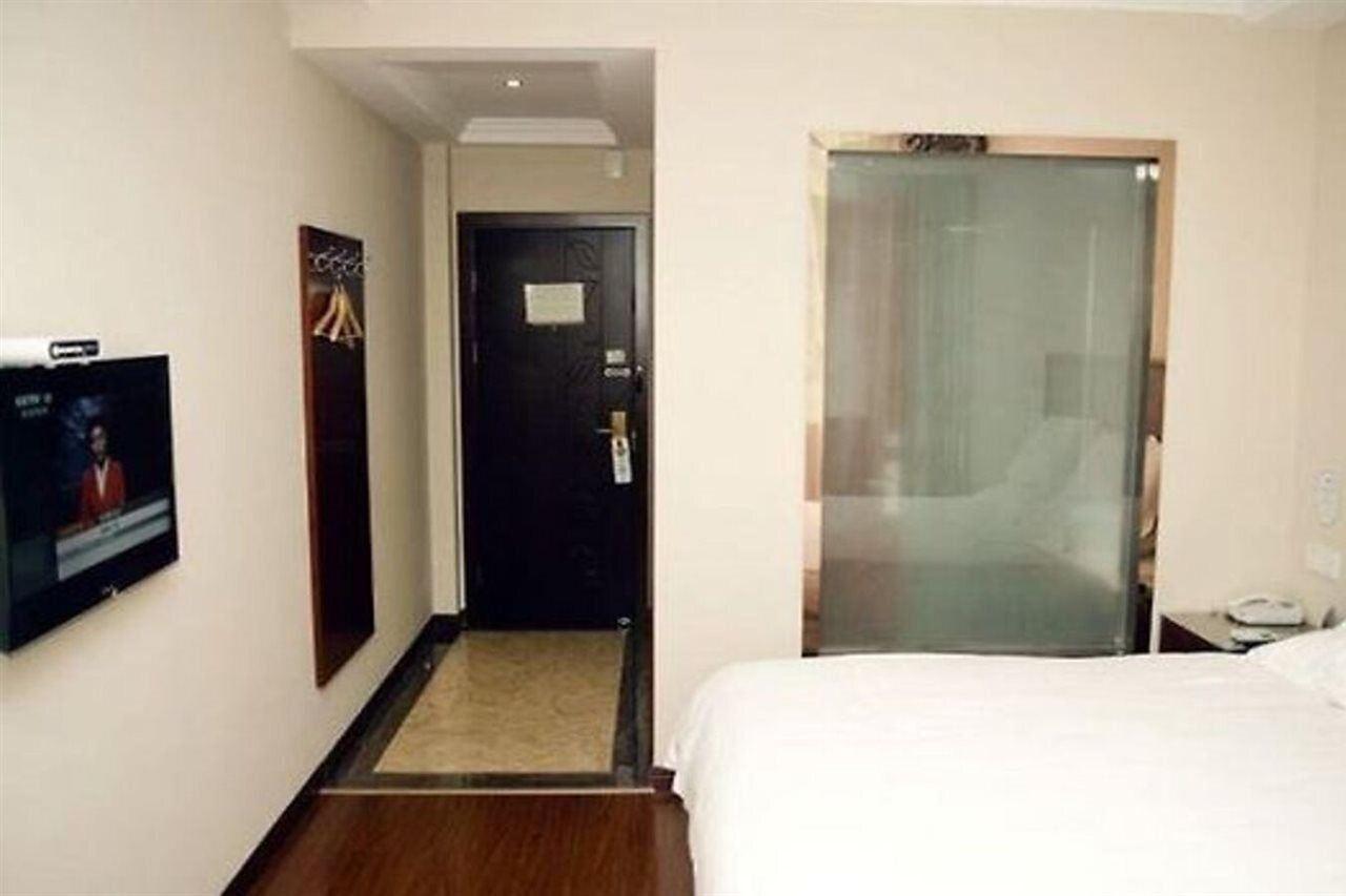 A hotel room with a bed, a TV mounted on the wall, a door, and a glass partition.