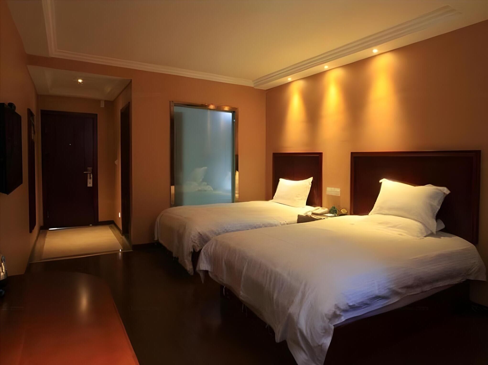 A hotel room with two beds, a door, and a wall-mounted TV.