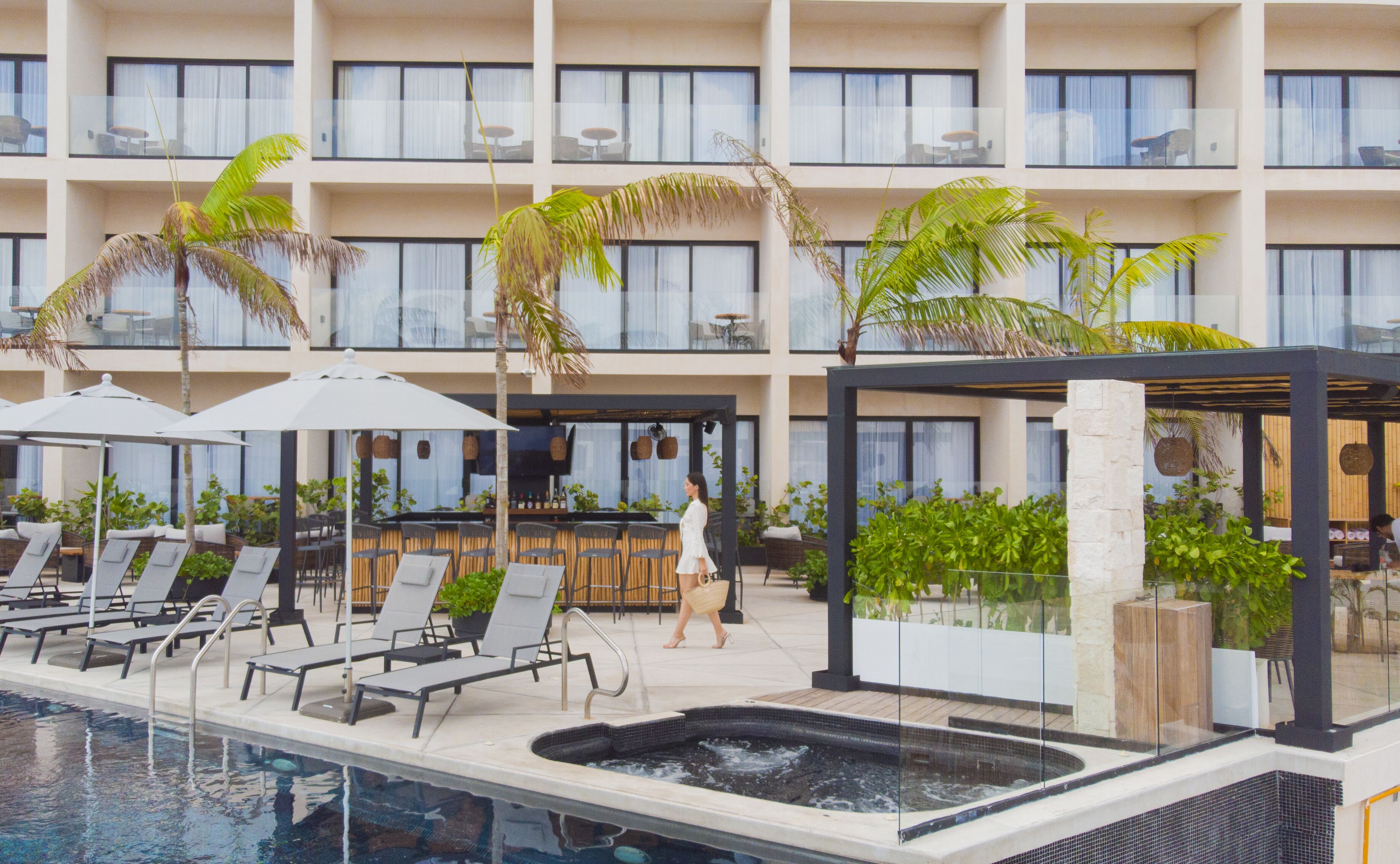 A pool area with lounge chairs, a hot tub, and a bar area with umbrellas.