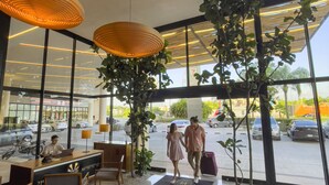 Un moderno vestíbulo de hotel con grandes ventanales, un mostrador de recepción, zona de estar y lámparas decorativas colgantes.
