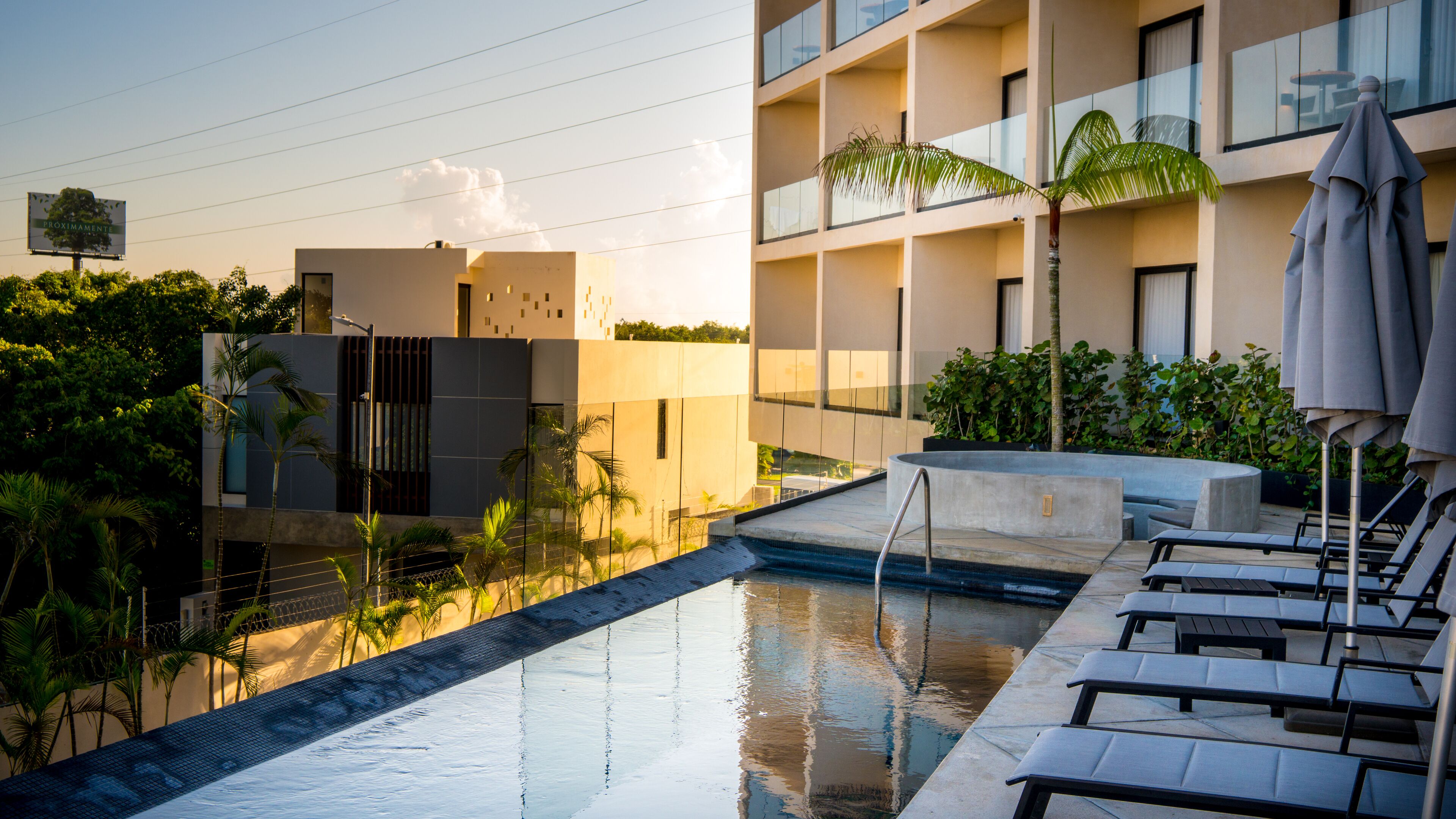 A modern hotel with a swimming pool, lounge chairs, and a view of the surrounding greenery and architecture.