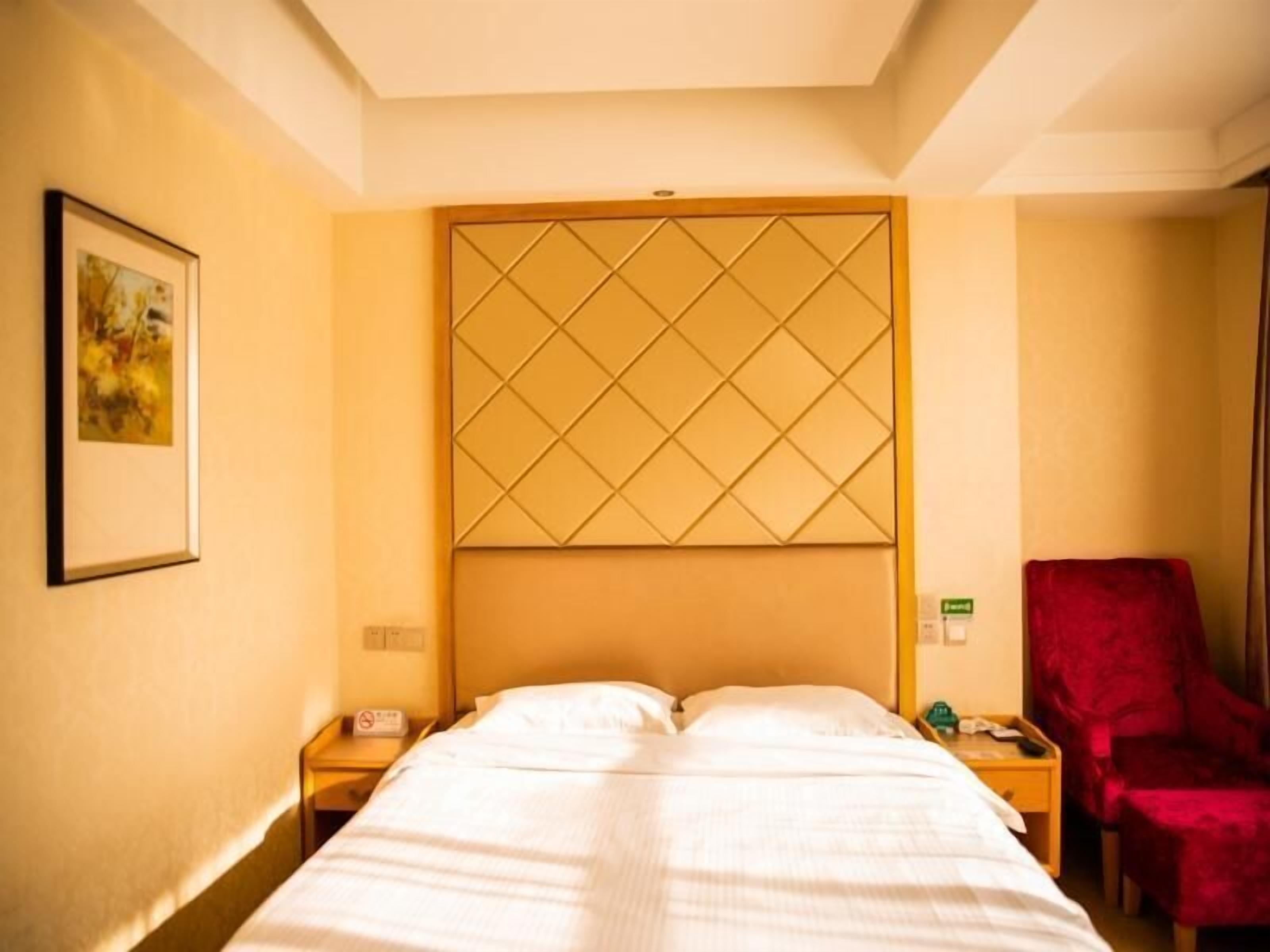 A hotel room with a bed, a nightstand, a red chair, and a wall-mounted artwork.