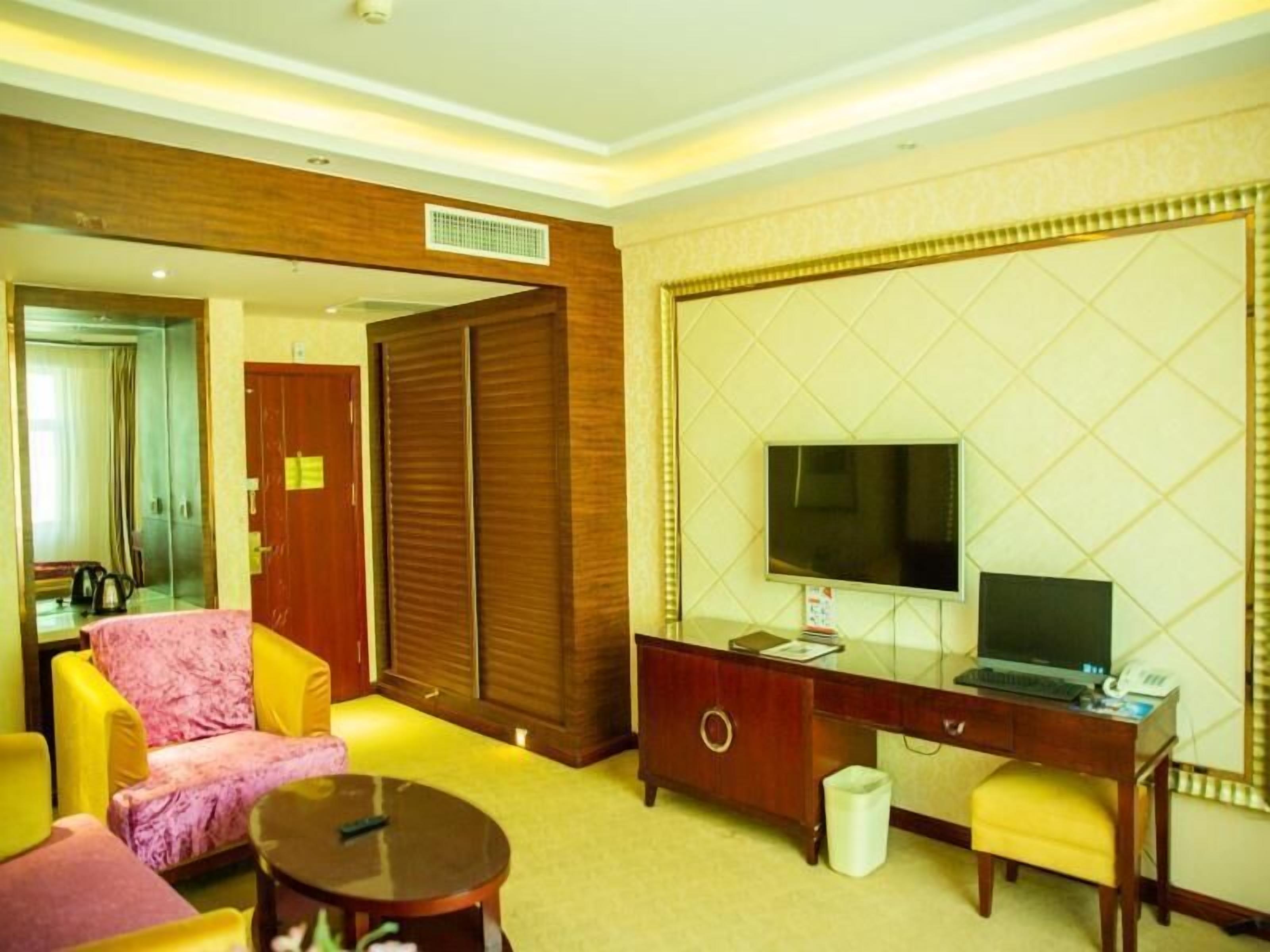 Una camera d'albergo con un letto, una scrivania con un computer, una TV e un'area salotto con poltrone.