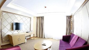 Ein Hotelzimmer mit einem großen Fernseher, einer Couch, einem Couchtisch und einem Schrank.
