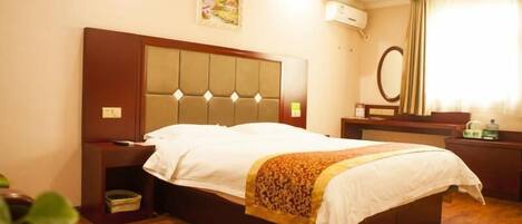 A hotel room with a large bed, a wooden headboard, a bedside table, a nightstand, a mirror, and a wall-mounted air conditioning unit.
