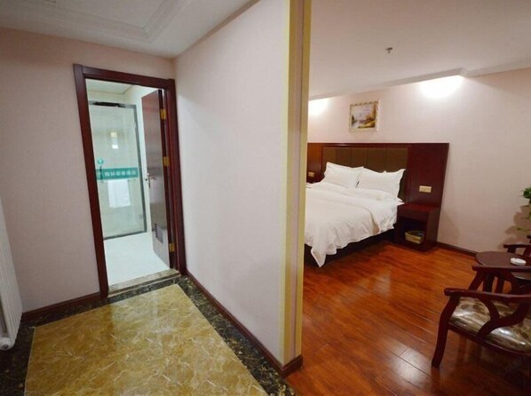 Habitación de hotel con piso de madera, una cama con ropa de cama blanca, una mesita de noche pequeña y una silla con cojín.
