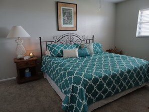 Relax in this serene bedroom with a neatly made bed, a framed art piece, and a cozy bedside table.