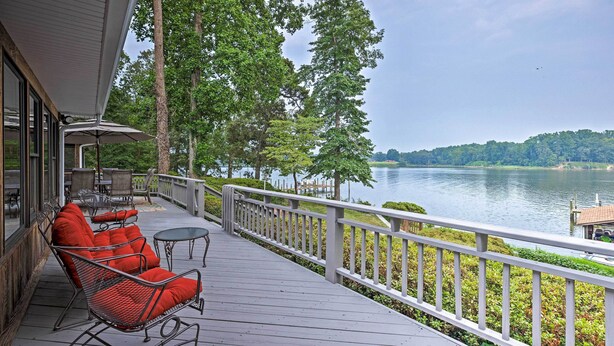 Une terrasse en bois, dotée de meubles d’extérieur, d’une rambarde et offrant une vue sur un lac et des arbres.