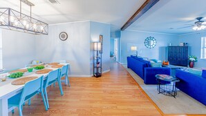 En rummelig opholdsstue med spisebord, blå stole, en blå sofa og en loftsvifte.