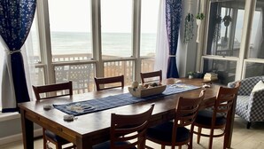 Un comedor con una mesa y sillas de madera, ventanas amplias con vista al mar y una alfombra estampada.
