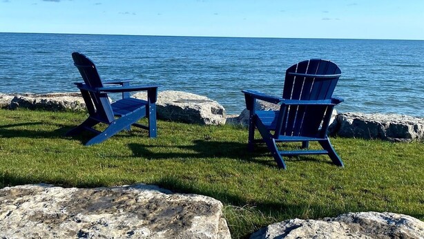 Dos sillas Adirondack mirando un cuerpo de agua bajo un cielo despejado.