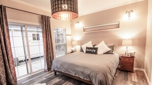 A bedroom with a large bed, a nightstand, a lamp, and a view of the outside through a sliding glass door. - Spacious Retreat with 2 Master Suites, Foosball & AC (Flagstaff)
