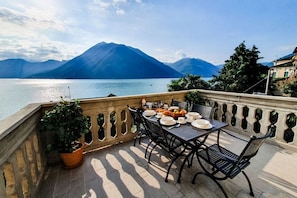 A terrace with a table set for dining, overlooking a lake with mountains in the background.