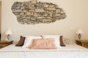 A bedroom with a stone wall, a bed with white and brown bedding, and two bedside tables with lamps.