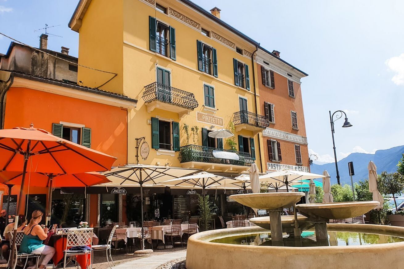 A café with outdoor seating, a fountain, and a yellow building with a sign reading "Caffè Rist."