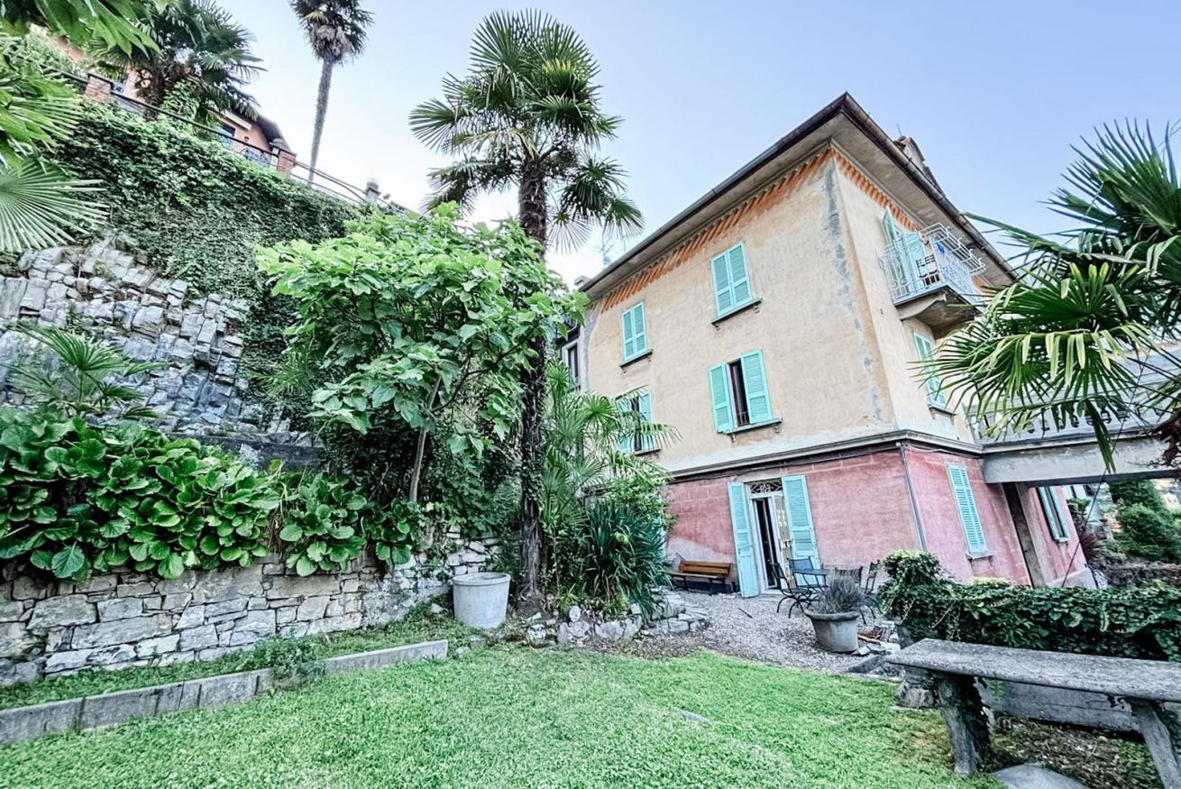 A two-story building with a stone wall and lush greenery.