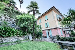 A two-story building with a stone wall and lush greenery.