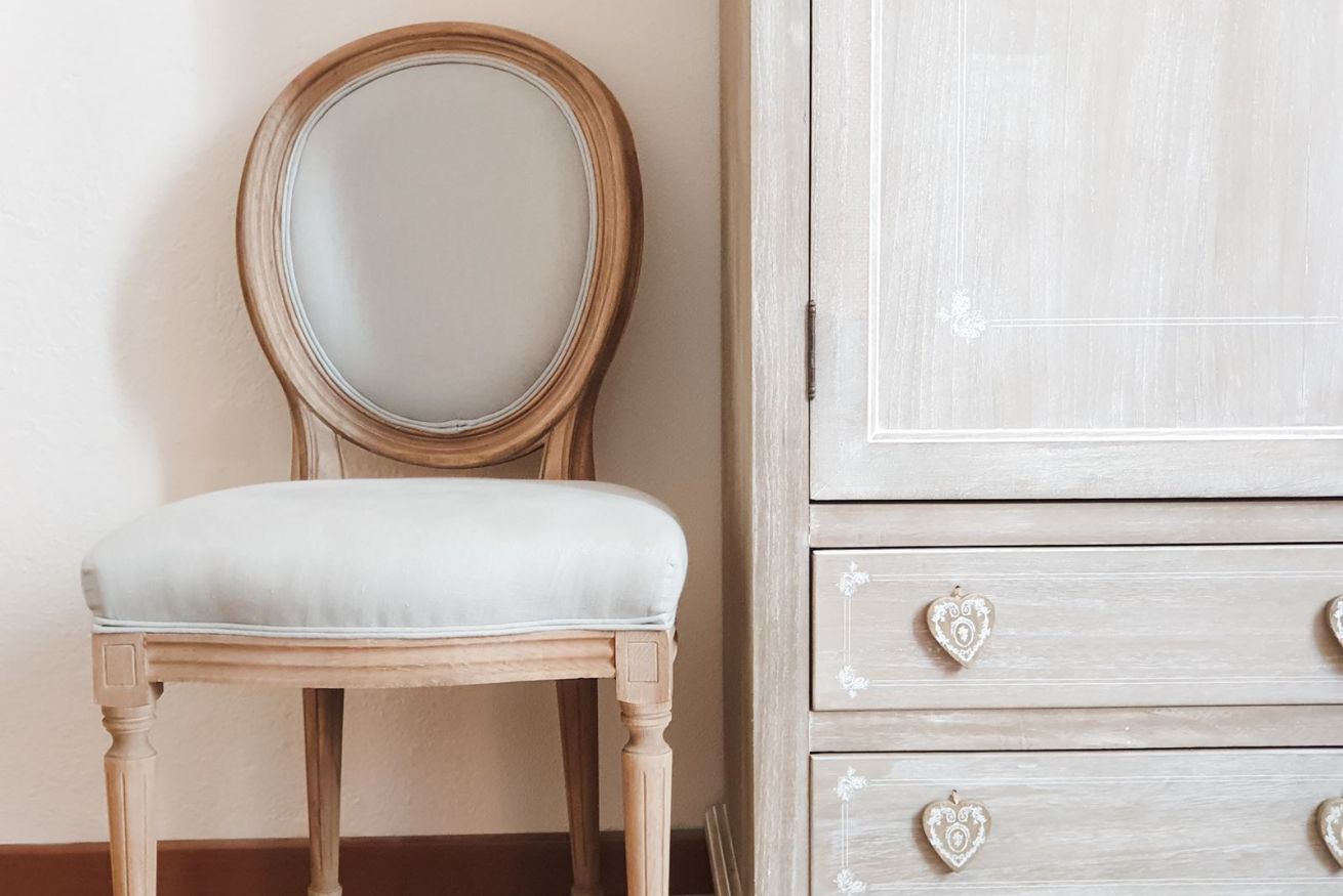 Une chaise en bois avec un siège rembourré et un miroir rond accroché au mur.