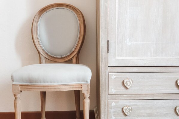 Una silla de madera con asiento acolchado y un espejo redondo en la pared.
