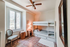 A bedroom with a bunk bed, a chair, a small table with a lamp, and a patterned rug.