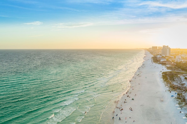 A coastal beach with a long stretch of sand, waves, and a cityscape in the background.