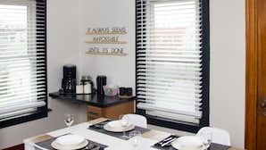 Un coin repas avec une table dressée pour quatre personnes, un espace dédié au café et une citation inspirante affichée sur le mur.