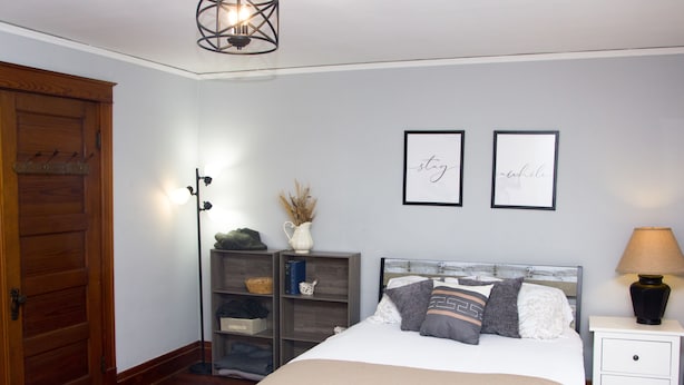 Une chambre à coucher comprenant un lit, des tables de chevet, une armoire, une lampe sur pied et des œuvres d’art murales.