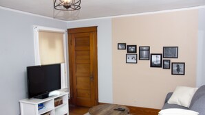 Un salon avec un téléviseur posé sur un meuble blanc, une porte en bois et un canapé avec des coussins.